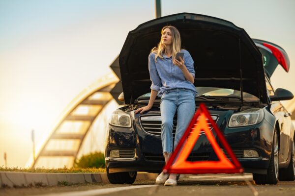 Femeie lângă mașină stricată cu triunghi reflectorizant